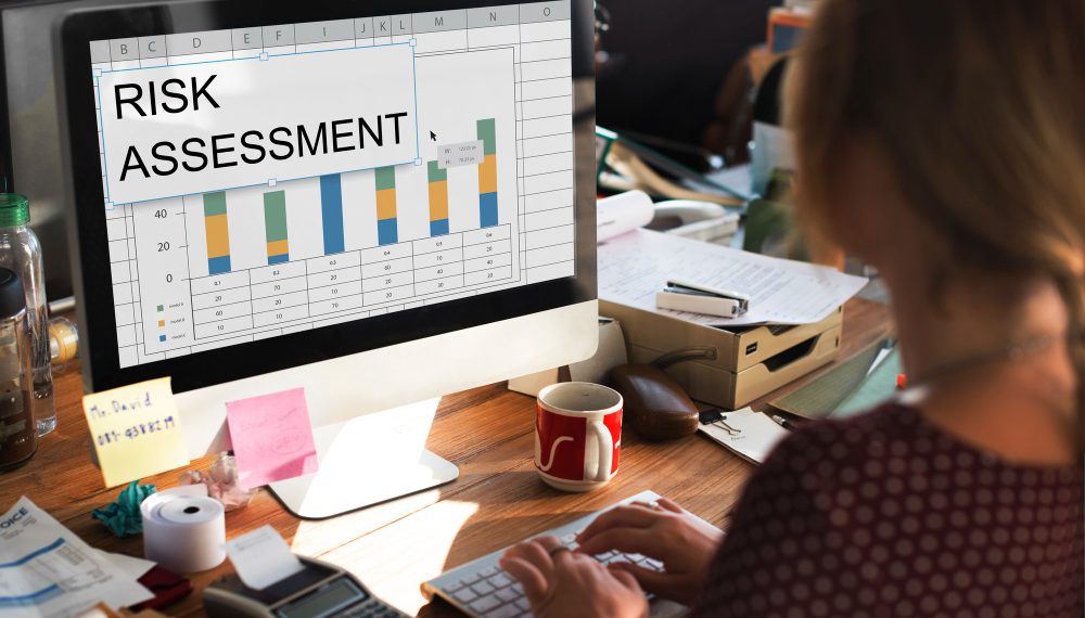 Person analysing a risk assessment chart on a computer screen in a busy office environment.