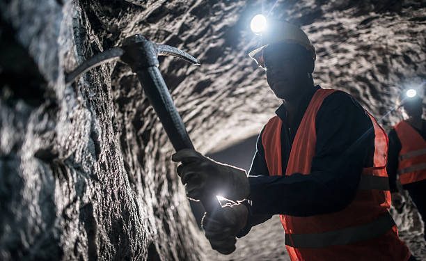 Underground miner wearing protective gear working below ground in a platinum mine.