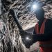 Underground miner wearing protective gear working below ground in a platinum mine.