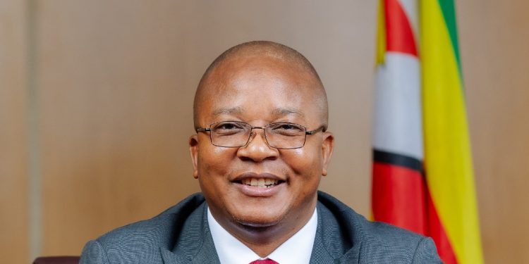 Zimbabwe Mines Minister Polite Kambamura seated at a desk with the national flag behind him.