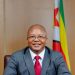 Zimbabwe Mines Minister Polite Kambamura seated at a desk with the national flag behind him.