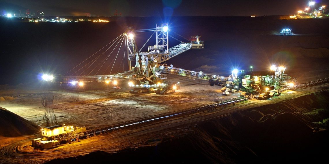 Open-pit mining operation at night with heavy machinery and conveyor systems illuminated by floodlights.
