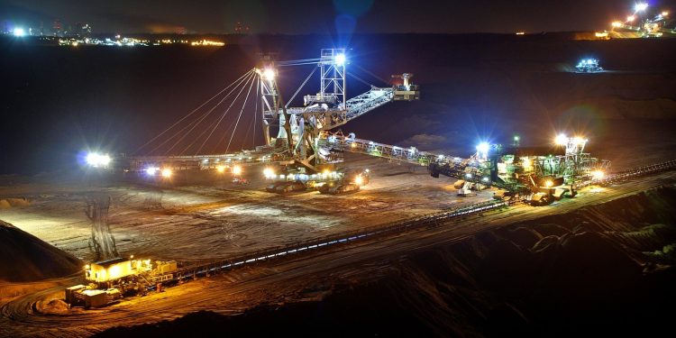 Open-pit mining operation at night with heavy machinery and conveyor systems illuminated by floodlights.