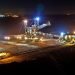Open-pit mining operation at night with heavy machinery and conveyor systems illuminated by floodlights.