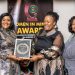Two women hold an award plaque during the Women in Mining Service Excellence Awards in Harare, with a banner in the background.