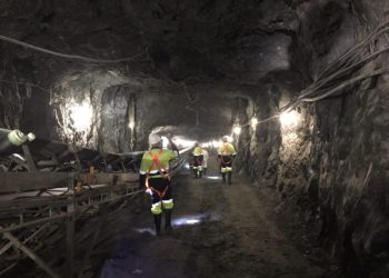 Underground mining tunnel at Blanket Mine in Zimbabwe, with workers in safety gear walking past conveyor systems.