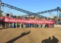 Workers stand in front of a spodumene lithium ore processing plant at the Bikita mine in Zimbabwe, holding a banner marking the project’s completion.