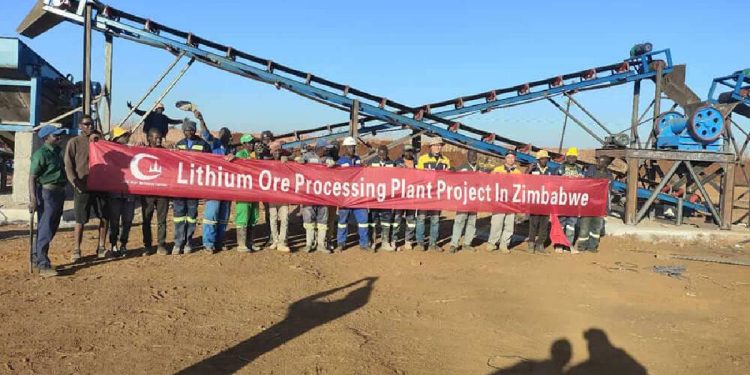 Workers stand in front of a spodumene lithium ore processing plant at the Bikita mine in Zimbabwe, holding a banner marking the project’s completion.