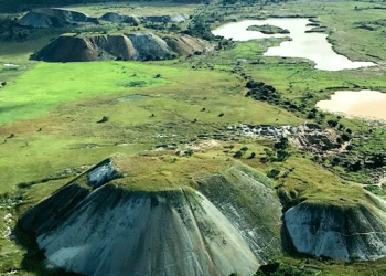 Aerial view of rounded mine waste mounds and surrounding green plains at the Manono Mine site.