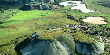 Aerial view of rounded mine waste mounds and surrounding green plains at the Manono Mine site.