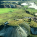 Aerial view of rounded mine waste mounds and surrounding green plains at the Manono Mine site.