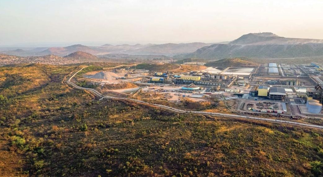 Aerial view of large industrial plant with warehouses and processing units surrounded by green hills.
