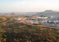 Aerial view of large industrial plant with warehouses and processing units surrounded by green hills.