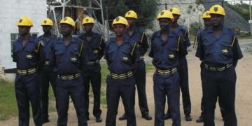 Mine security guards in blue uniforms and yellow helmets stand in formation at an industrial site.