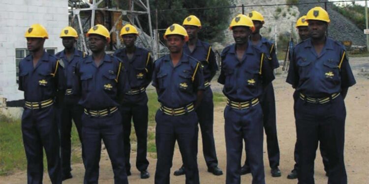Mine security guards in blue uniforms and yellow helmets stand in formation at an industrial site.