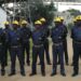 Mine security guards in blue uniforms and yellow helmets stand in formation at an industrial site.
