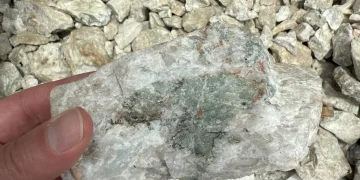 Close-up of a hand holding a white and green lithium-bearing rock sample over crushed stones at the Fonlo Project in Nigeria.