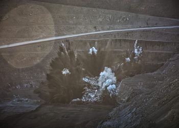 A controlled explosion in an open-pit mine sends dust and debris into the air.