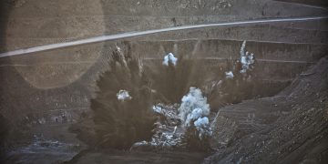 A controlled explosion in an open-pit mine sends dust and debris into the air.