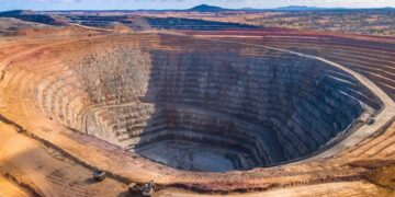 Aerial view of an open pit mine in Africa showing terraced rock walls and heavy equipment at the base