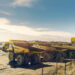 A row of large haul trucks parked at an open-pit mine, with additional mining vehicles and earthworks visible in the background.