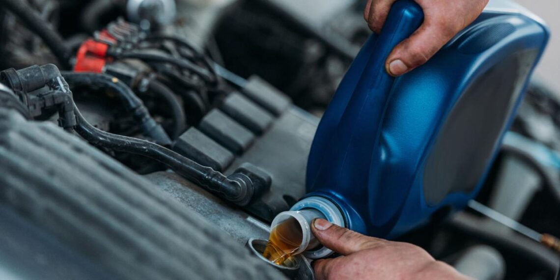 A mechanic pours engine oil into a vehicle engine during maintenance.