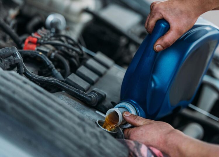 A mechanic pours engine oil into a vehicle engine during maintenance.