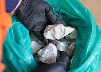 A gloved hand holds a sample of spodumene ore, a lithium-bearing mineral.