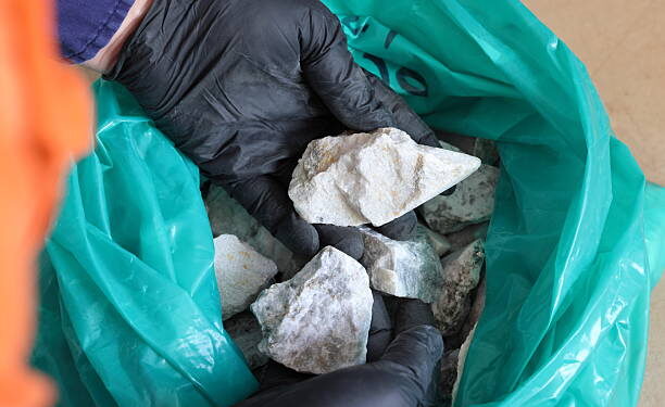 A gloved hand holds a sample of spodumene ore, a lithium-bearing mineral.