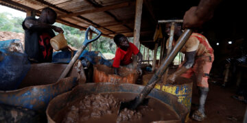 A young artisanal miner washes crushed rock containing gold in metal drums at the unlicensed mining site of Nsuaem Top in Ghana