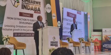 Minister Polite Kambamura speaks at a podium during the Zimbabwe Alternative Mining Indaba, with banners showing the event theme on sustainable development.