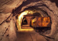 A rusted ore cart on rail tracks inside an underground mine tunnel