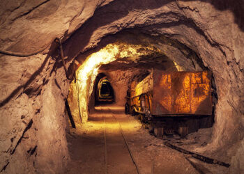 A rusted ore cart on rail tracks inside an underground mine tunnel