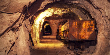 A rusted ore cart on rail tracks inside an underground mine tunnel