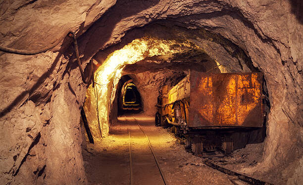 A rusted ore cart on rail tracks inside an underground mine tunnel