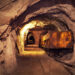 A rusted ore cart on rail tracks inside an underground mine tunnel