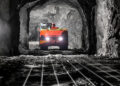 Underground mining truck travelling through a mine tunnel illuminated by vehicle headlights.